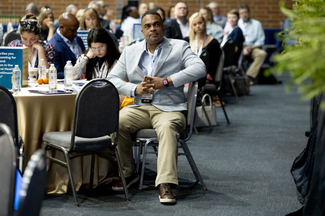 Audience members sit around a table and listen to presentation dressed in business casual attire