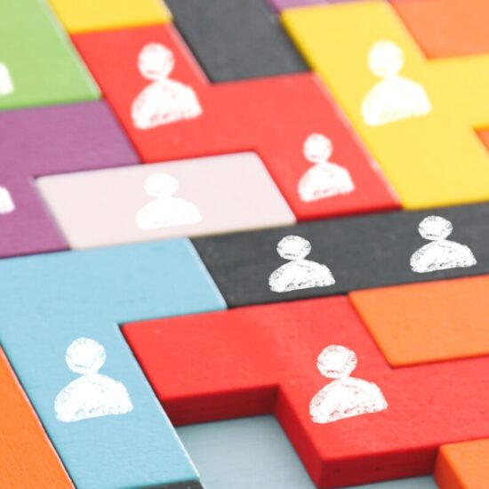 mutil-colored tangram puzzle blocks with people icons over wooden table. one piece is missing